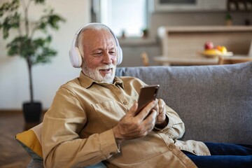 Senior man wearing headphones listens to favorite Mp3 digital music on smartphone at home while...