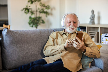 Shot of a senior man using headphones and a smartphone on the sofa at home.