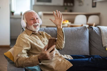 Fotobehang Phone, senior man and watch music video, streaming podcast and reading happy story, news article or retirement blog. Home, smartphone and elderly person with headphones, relax and listening to song. © Jelena Stanojkovic