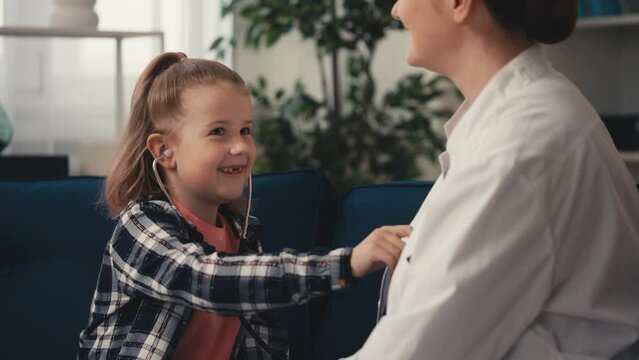 Smiling girl listening to doctor mom's lungs with stethoscope, playing doctor