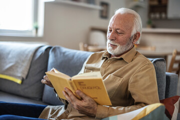 Senior men enjoying time at home by reading his favorite book. - obrazy, fototapety, plakaty
