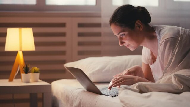 Young woman working on laptop in bed, embodying the freelancer lifestyle