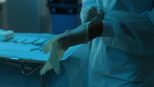 Close-up hands of unrecognizable African-American doctor or nurse worker surgeon preparing for surgical operation and wearing hand gloves at health clinic or hospital office. Shooting in slow motion.