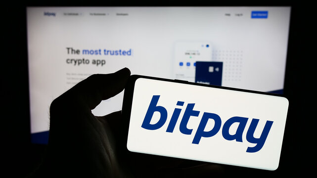 Stuttgart, Germany - 12-18-2023: Person holding smartphone with logo of US cryptocurrency payment company BitPay Inc. in front of website. Focus on phone display.