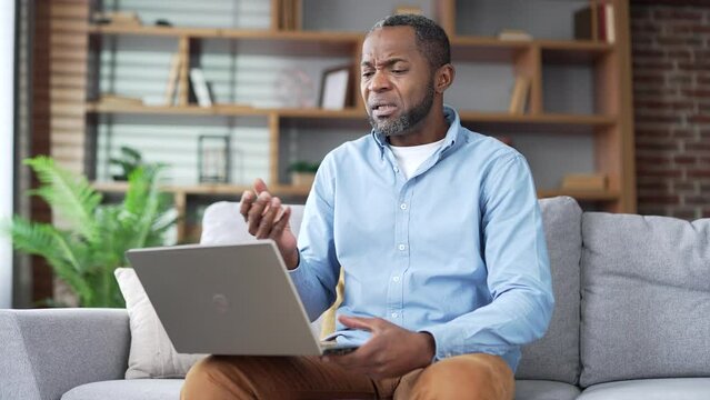 Mature african american male talking on video call with a psychologist or doctor using laptop sitting on sofa at home. Senior black man complaining about his problems illness at an online consultation