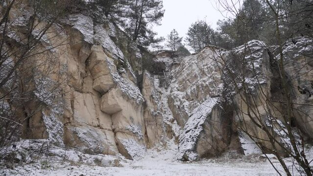 Scenic winter landscape with falling white snow, tall coniferous trees and ice capped rocks. Leisure time spending in nature during cold season far beyond big cities. Concept of weather and view.