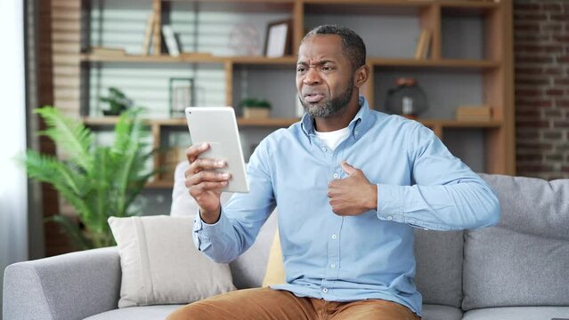 Mature african american male having a video call with a doctor using digital tablet sitting on sofa in living room at home. Sick senior black man telling about his problems, complaining about illness