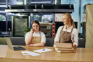 young woman with down syndrome talking on smartphone near laptop and cafe manager with pizza boxes