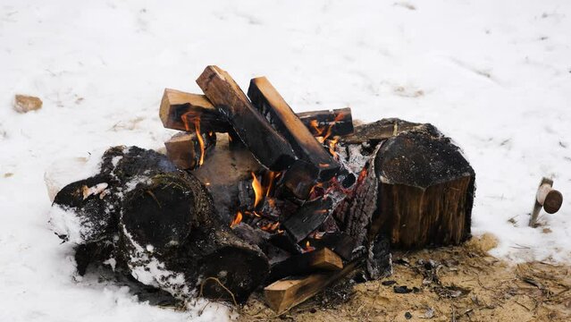 Self-made fire from chopped burnt wood flaring up and smoking among white winter snow on wild nature. Place in campsite for warming up and heating food or drinks. Concept of hiking and leisure.