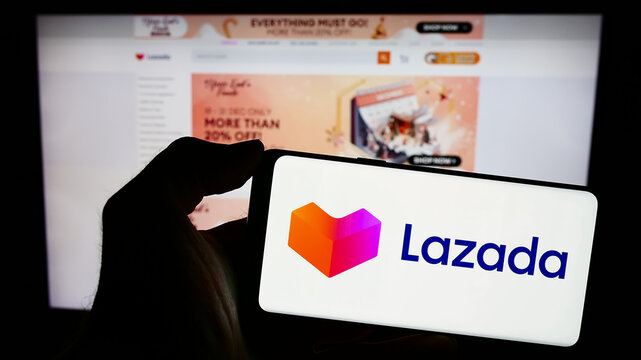 Stuttgart, Germany - 12-20-2023: Person holding mobile phone with logo of Asian e-commerce company Lazada Group in front of business web page. Focus on phone display.