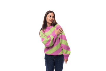 well-groomed slim young european brunette woman dressed in a striped pink-green pullover on a studio background