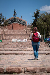 Mujer turísta caminando por la ciudad de Humahuaca, en la plaza central con cartel turístico.	