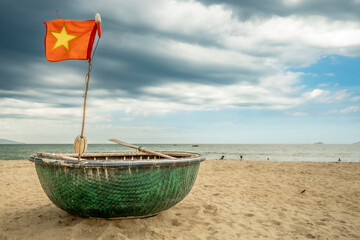 Traditional Vietnamese round fishing boat on the beach at Hoi An, with the Vietnam flag flying. 