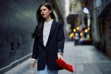 Obraz premium Fashion woman tourist in stylish clothes in a jacket and red beret walking down a narrow city street flying hair and happy travel, French style, cinematic color, retro style.