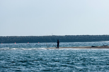 Obraz premium A lone fisherman stands at the seashore, casting his line into the rhythmic dance of the waves. The rhythmic sound of waves crashing on the shore provides a soothing backdrop to his patient endeavors.