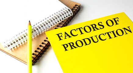 FACTORS OF PRODUCTION text written on a yellow paper with notebook