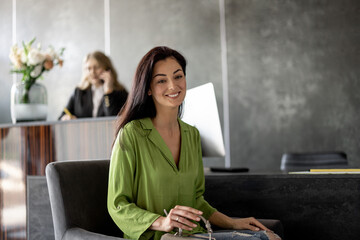 Cheerful woman sitting at reception desk of a modern clinic. Medical receptionist on background....