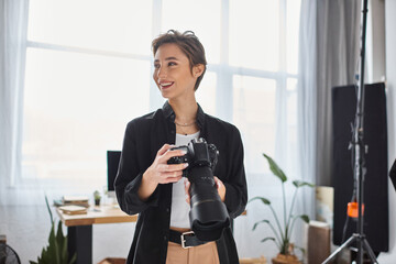 merry female photographer in casual clothes with camera in her hands smiling and looking away - Powered by Adobe