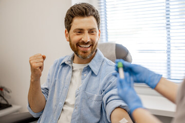 Happy man gives blood for tests in laboratory, medical worker holds test tube filled with blood in...