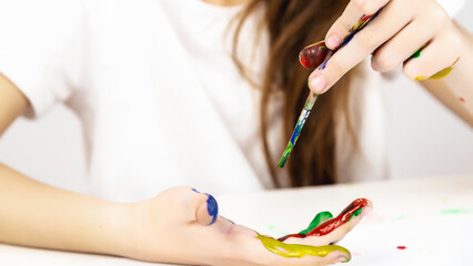 Childish pranks. Child with painted palms with multicolored paints. A little girl happily draws with her hands.