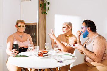 Group of adult men drag queens sitting at table and friend checking messages on smartphone