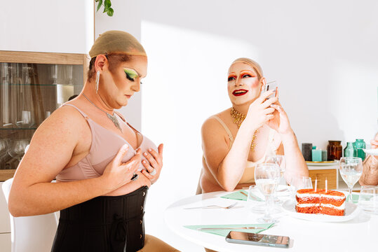 Adult men drag queens sitting at table talking and adjusting bra