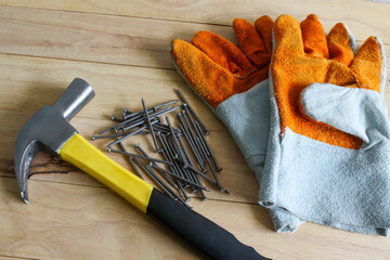Hammer, nails, and gloves are tools for general construction work on a wooden background.