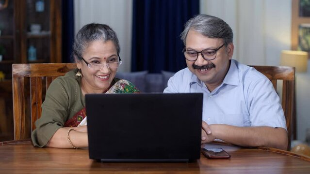 An aged Indian husband-wife doing a video call on a laptop - use of technology  internet penetration  4g  5g  talking to overseas family. A happy elderly couple waving while chatting online - dista...