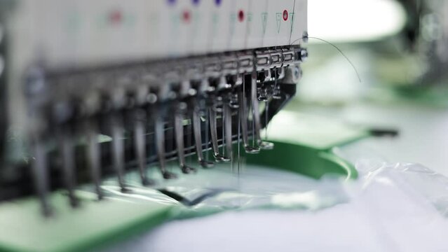 Close up of automatic embroidery machine needles stitching logo on white fabric in textile industry at garment manufacturer. Modern equipment decorating cloth without direct human participation.