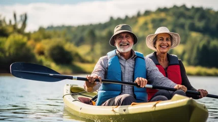 Foto op Canvas pareja de hombre y mujer seniors navegando en canoa por un lago entre montaÃ±as en un dÃ­a soleado, concepto de vacaciones y actividades para mayores © sambath