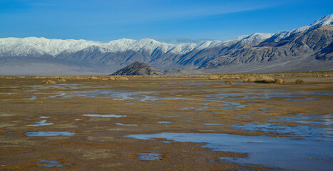 Landscape of wet clay desert in winter against the backdrop of snow-capped mountains in the Death Valley area
