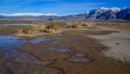 Landscape of wet clay desert in winter against the backdrop of snow-capped mountains in the Death Valley area