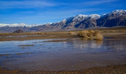Landscape of wet clay desert in winter against the backdrop of snow-capped mountains in the Death...