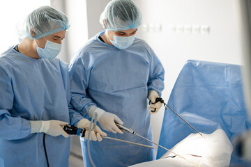 Two surgeons in uniform stand with endscopes preparing for minamal invasive procedure for a patient...