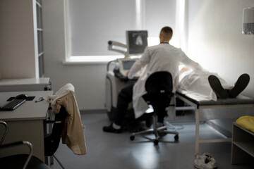 Ultrasound specialist examining male patient in medical office, wide view on medical room where the diagnostic procedure takes place