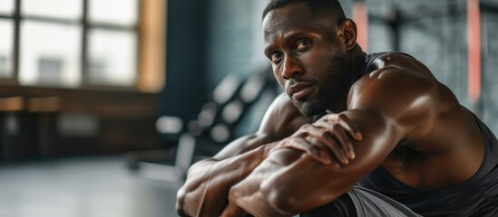 A black man stretches in the gym to warm up and improve his health and flexibility before a workout. - obrazy, fototapety, plakaty