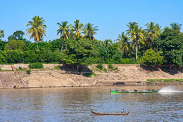 a green speedboat cruises fast down a river on a shore planted with palm trees and blue sky