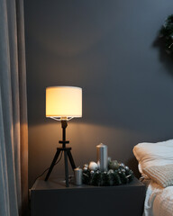 There is a nightstand in the room next to the bed, a nightlight on the nightstand. Gray wall, lamp...