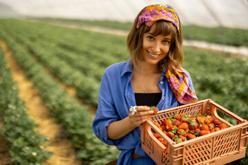 Portrait of a young stylish woman standing with basket full of fresh picked up strawberries in...