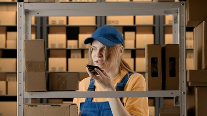 Portrait of female model working in storage. Girl storekeeper in uniform near rack with boxes,...