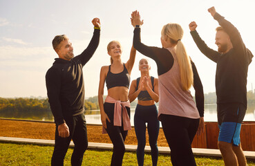 Portrait of group of sport friends standing in the park, exchanging high fives with radiant smiles....