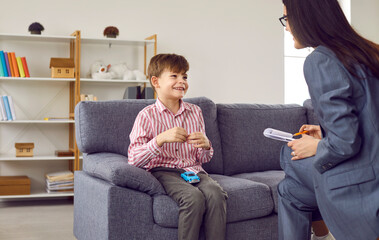 Young female psychologist having conversation with smiling little boy during meeting. Cute boy...