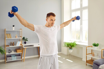 Portrait of sporty handsome young man wearing white T-shirt doing sport exercises at home raising...