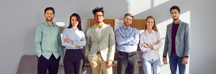 Fototapeta premium Banner with a portrait of a diverse business team. Group of young multiracial people standing together by the wall in the company office. Teamwork, success, professional leadership concepts