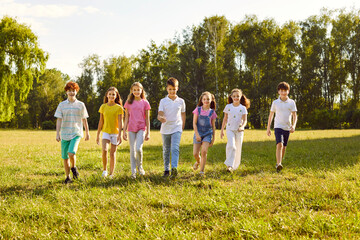 Happy children walking in a line together outside and smiling in the park on holidays enjoying spending time in a summer camp. Full length portrait of a kids having a walk in nature. - obrazy, fototapety, plakaty
