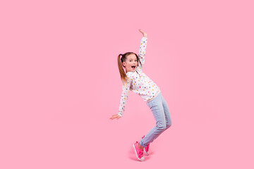 Full size photo of cute schoolgirl dressed dotted pullover denim pants stand on tiptoes near empty space isolated on pink color background
