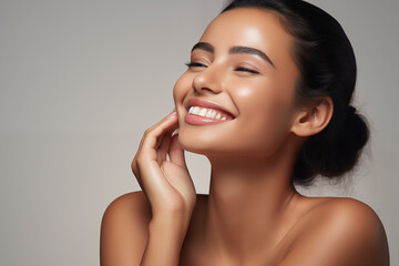 Beautiful laughing young Indian woman takes care of her skin, posing over grey background