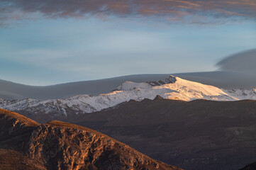Naklejka premium Sunset with spectacular lenticular clouds in the sky over the snowy peaks of Sierra Nevada (Granada, Spain)