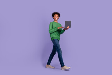 Fototapeta na wymiar Full length photo of funny positive man dressed green sweater walking texting modern device empty space isolated violet color background
