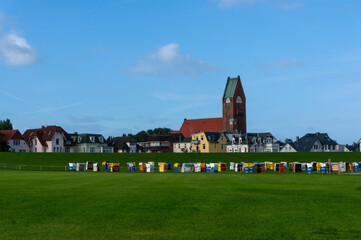 Parish Church of Saint Peter (St. Petri) in background, it was garrison church, built  in 1911. Unused hooded beach chairs (strandkorb) on green grass field. Cuxhaven, Germany. - obrazy, fototapety, plakaty
